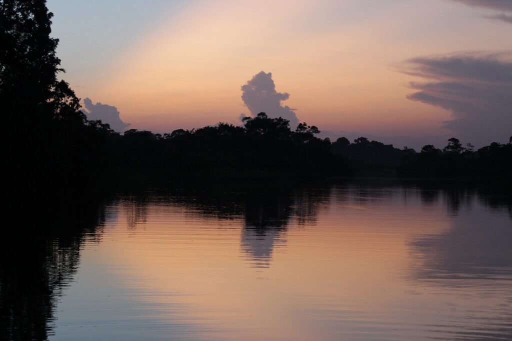 Dusk on a river. The dull pink sky is reflected in the still water. Wheely Tyred Ecuadorian Amazon safety
