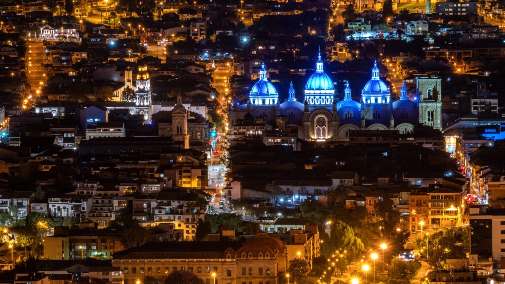 An aerial shot of a city at night, showing blue domes on a cathedral in Cuenca, Ecuador.