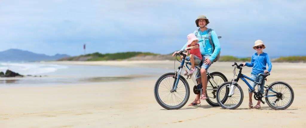 A family cycles along a beach on the Galapagos Islands.
