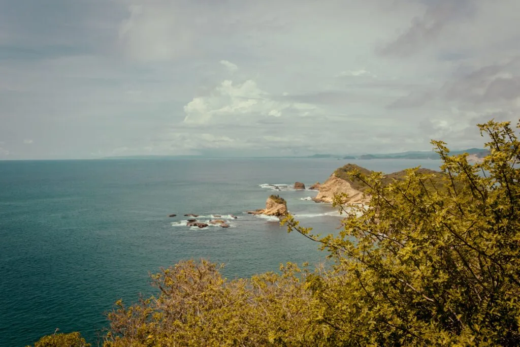 A headland on Los Frailes Beach can be seen with waves breaking against it.