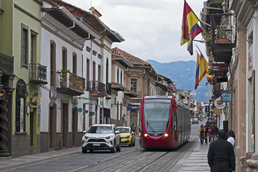 A red tram runs through a colonial street in Cuenca, Ecuador.