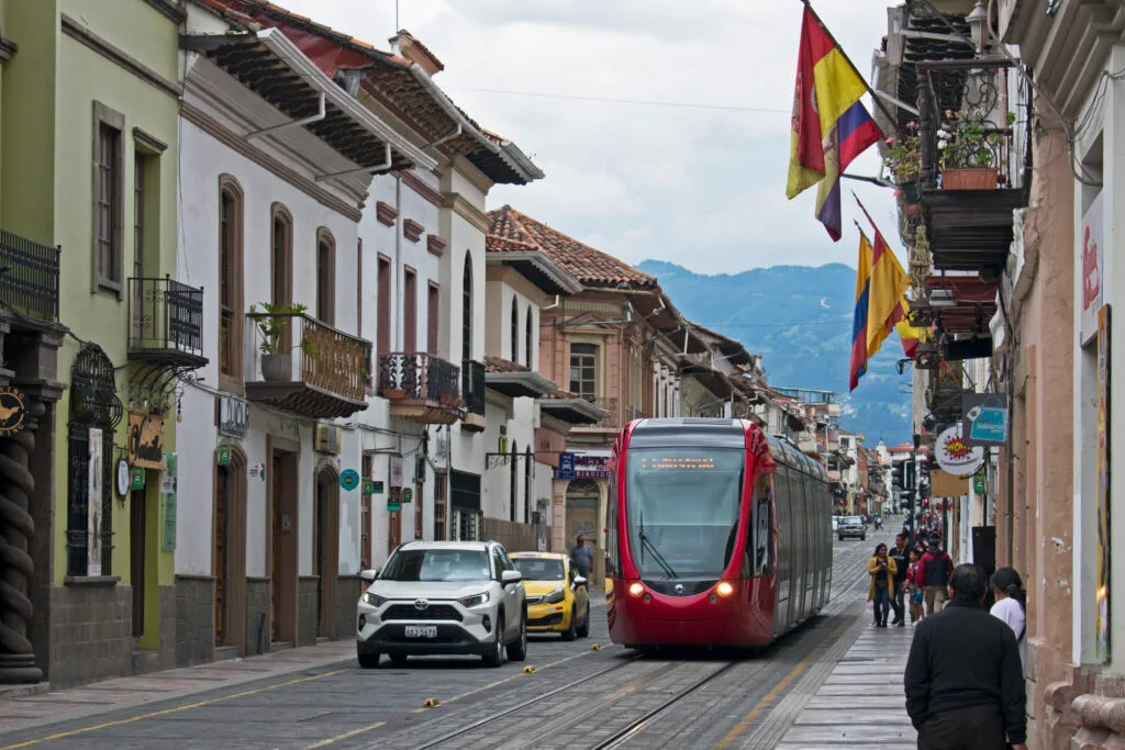 A red tram runs through a colonial street in Cuenca, Ecuador.