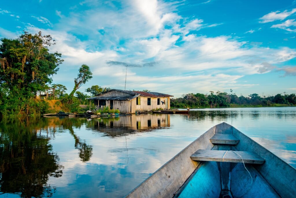 A boat floats towards a house built on stilts over a river in the Amazon Rainforest.