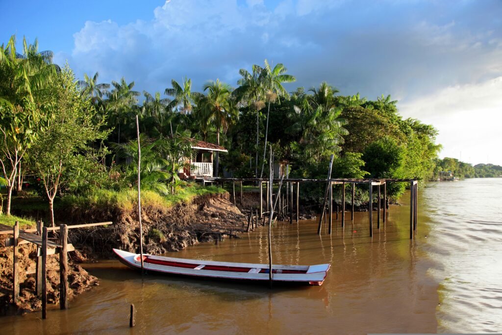 A boat is tied underneath a house, against a river bank in the Amazon rainforest. Wheely Tyred Cuyabeno