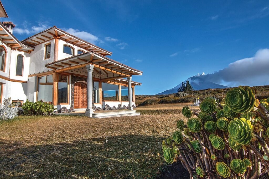 Smoke rises out of Volcán Cotpaxi with Hotel Hacienda Los Mortinos in the forgraound