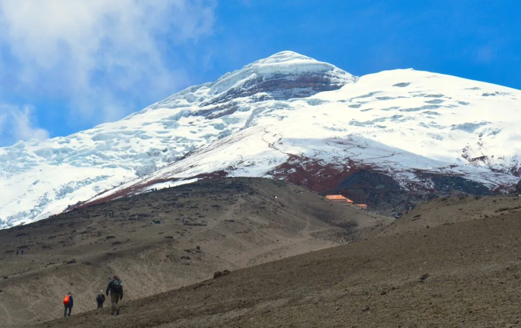 People walk towards the Refugio José Rivas on a sunny day on Cotopaxi, Ecuador.