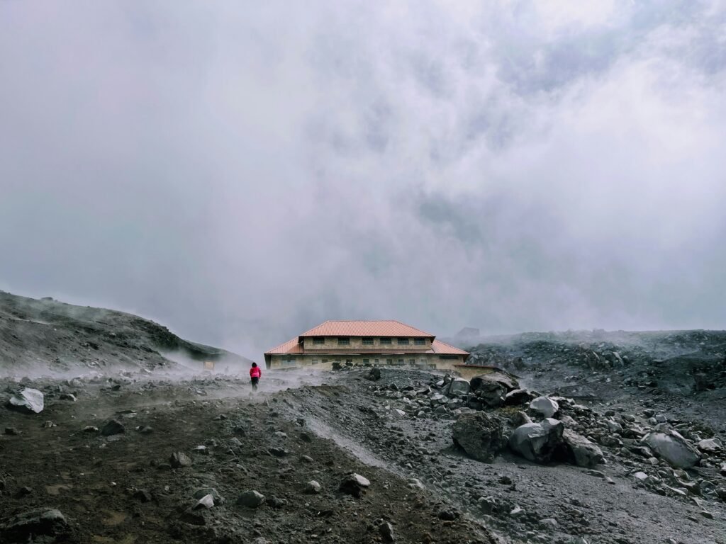 A person stnads in front of Refugio José Rivas surrounded by clouds on Cotopaxi, Ecuador.