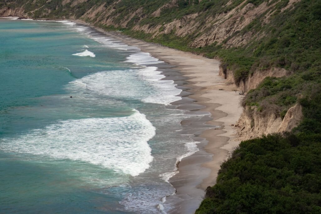 Waves crash against a beach with cliffs coming down to the shore in Manabí, Ecuador. Wheely Tyred Puerto López