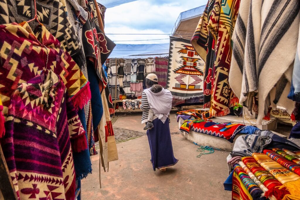 A woman carries a baby through the Plaza de Ponchos market selling indigenous crafts in Otavalo, Ecuador.