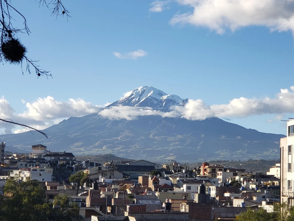 A snowcapped volcano rises out of the horizon, dwarfing a town in Ecuador