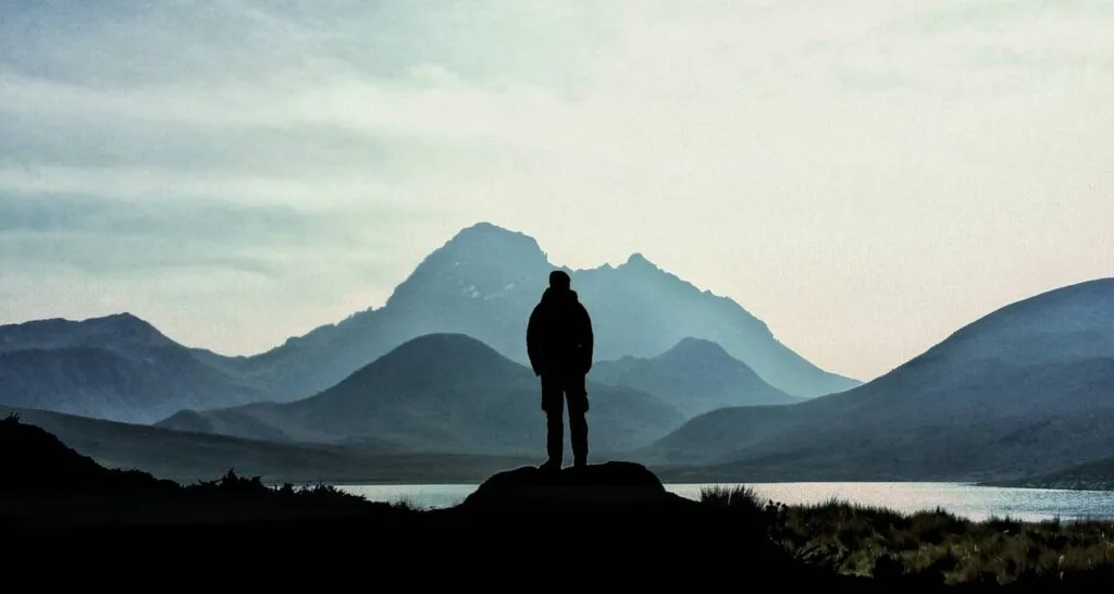 A silhouette of a man looks over a lake towards a volcano in Ecuador