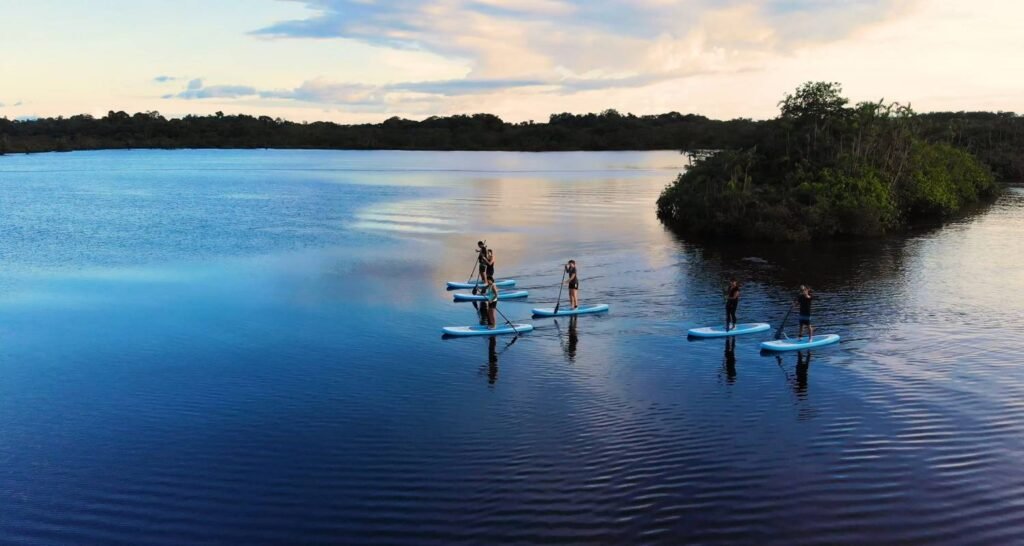 A group of people paddleboard along a river so still it’s like a mirror in the Amazon, near Cuyabeno, Ecuador