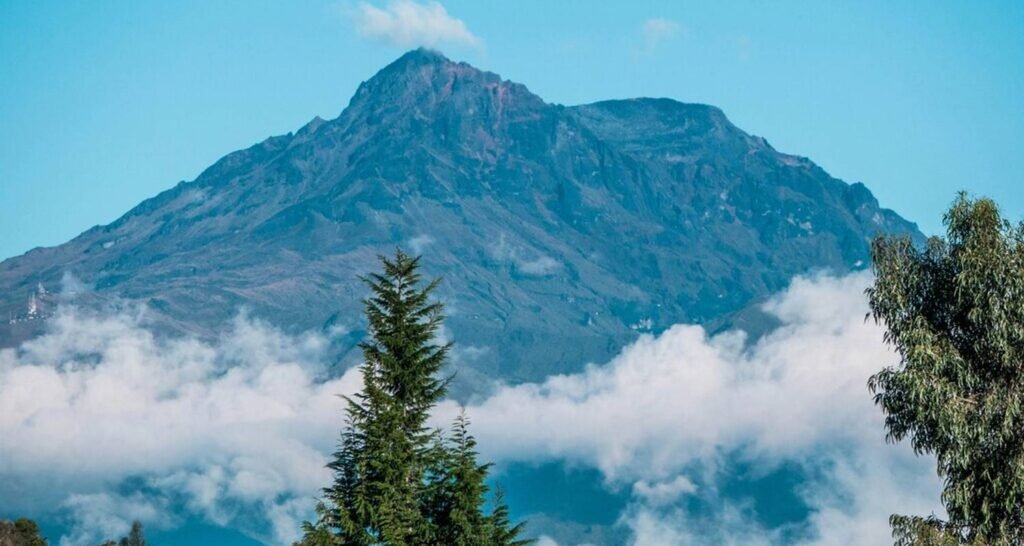 A huge volcan rises out of the clouds and trees in Ecuador
