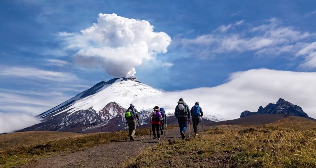 A group of people walk toward Cotopaxi, which has a large plume of smoke rising our of its crater, in Ecuador