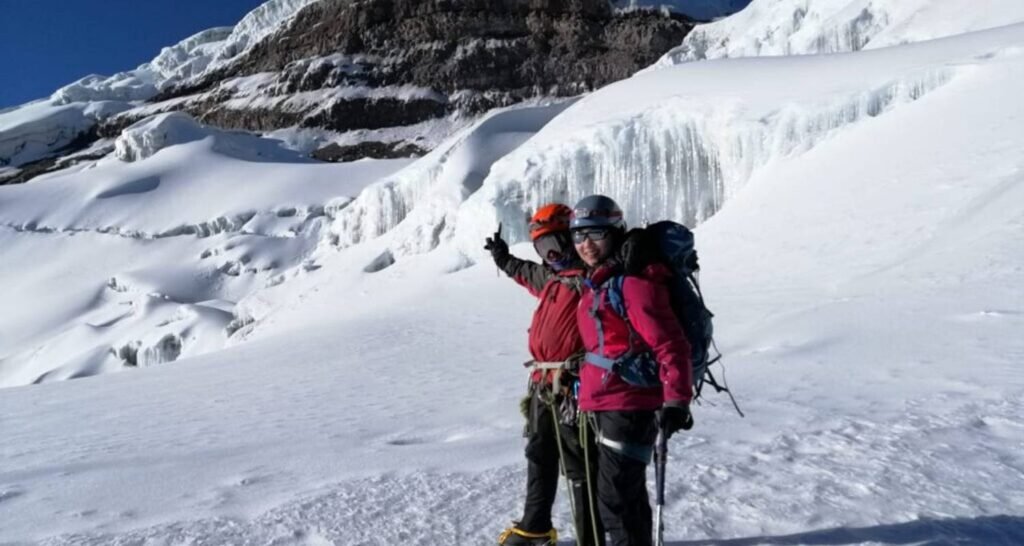 Two people in heavy cold weather clothes stand in the snow on top of Cotopaxi, Ecuador