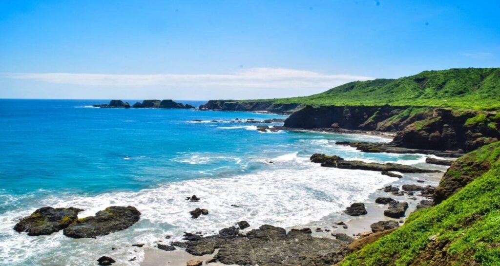 Waves crash into small cliffs under a blue sky in Ecuador