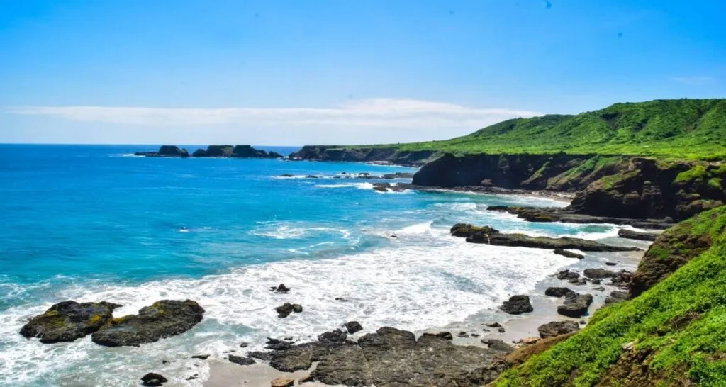 Waves crash into small cliffs under a blue sky in Ecuador