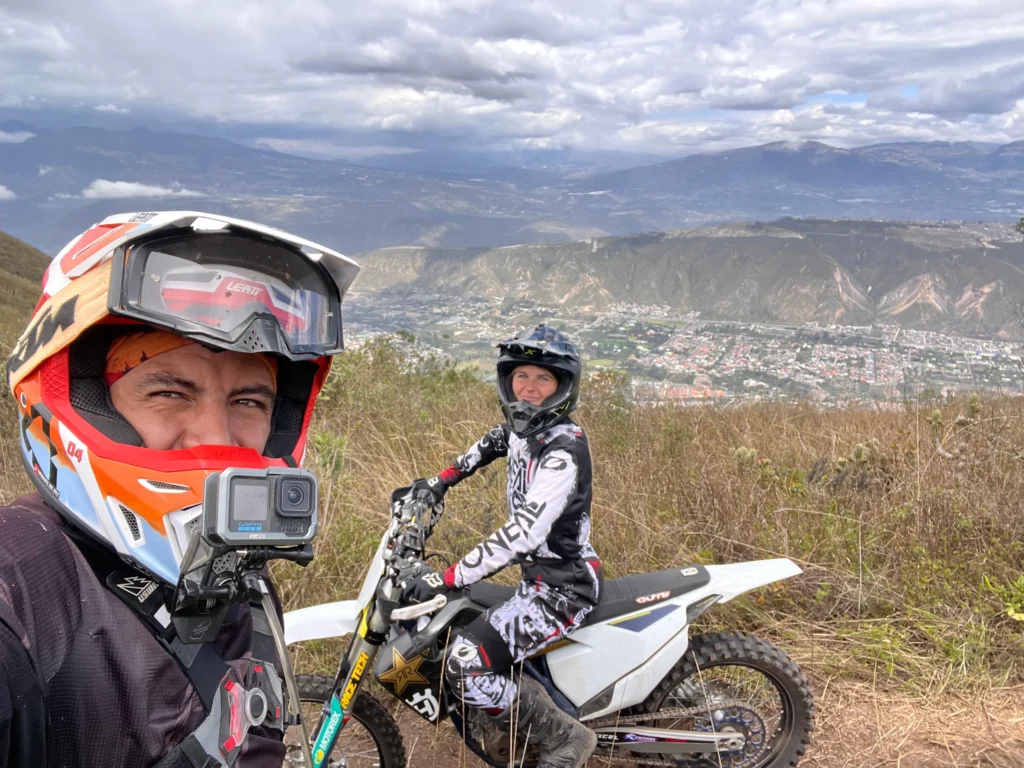Two people pose on motorbikes on a ridge high over Quito, Ecuador. Wheely Tyred Best Mindo bike tours