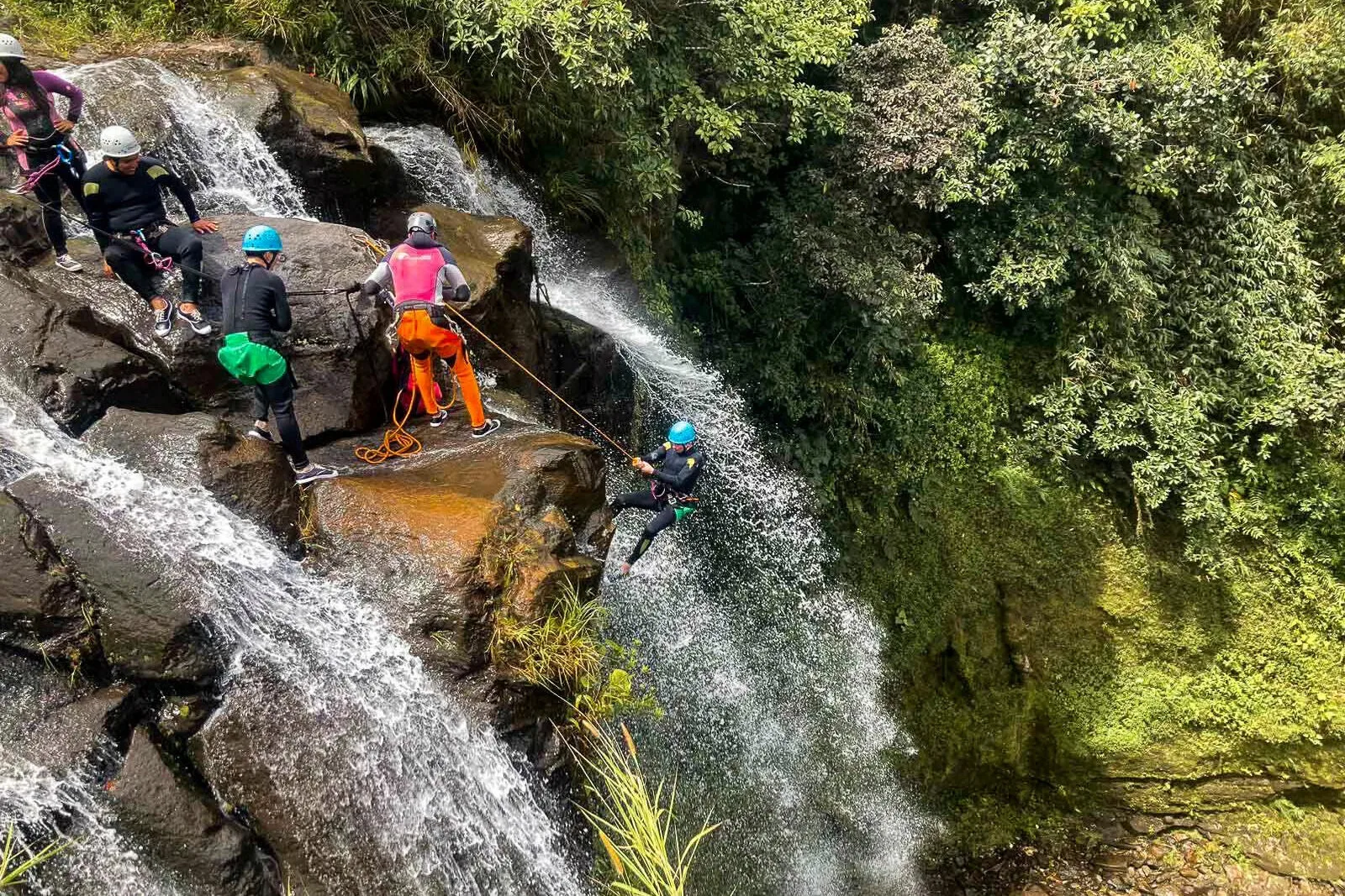 Someone abseils off the edge of a cliff with througha waterfall near Baños, Ecuador