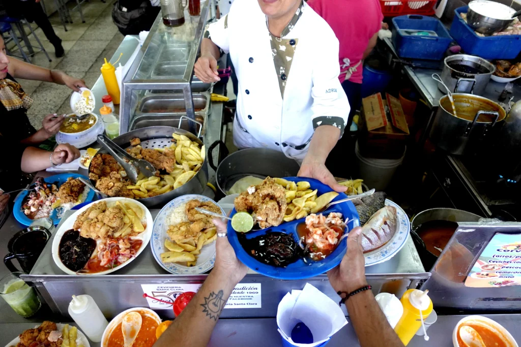 A vendor passes a plate of fried food over a counter in a market in Quito, Ecuador