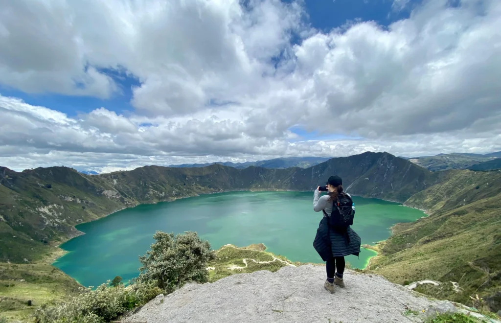 A woman takes a photo of the emerald caldera lake at Quilotoa, Ecuador