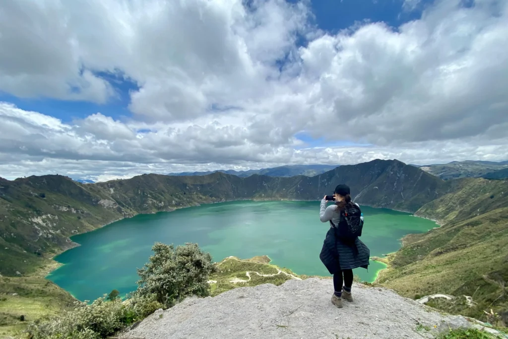 A woman takes a photo of the emerald caldera lake at Quilotoa, Ecuador