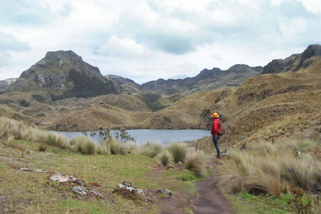 A person in red with a yellow hat stands beside one of the many lakes in Cajas National Park, Ecuador