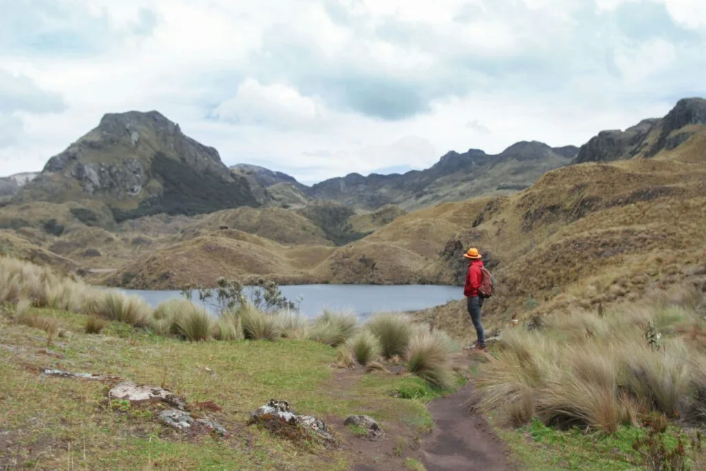 A person in red with a yellow hat stands beside one of the many lakes in Cajas National Park, Ecuador