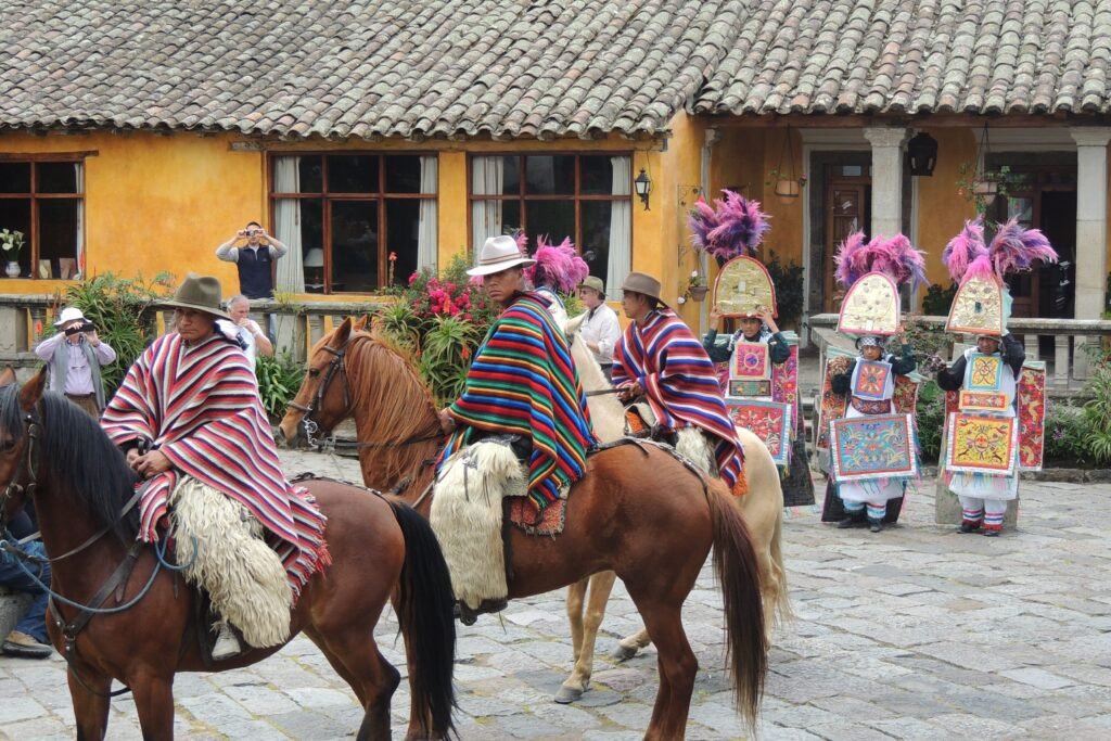 Indigenous people in ponchos ride horses at a house near Cotopaxi, Ecuador
