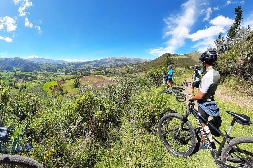 People on mountain bikes look over a valley of bright green fields in Ecuador. Wheely Tyred Best Otavalo bike tours