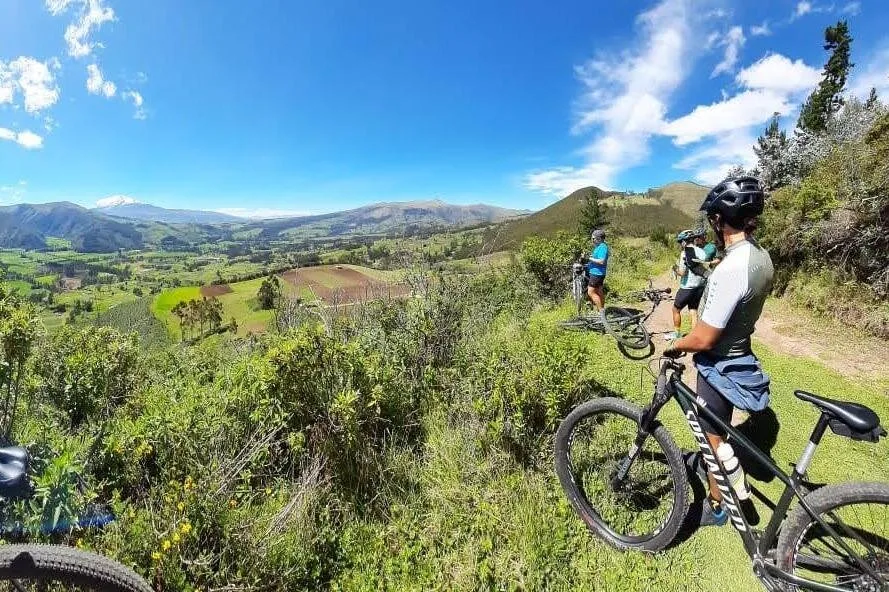 People on mountain bikes look over a valley of bright green fields near Otavalo, Ecuador