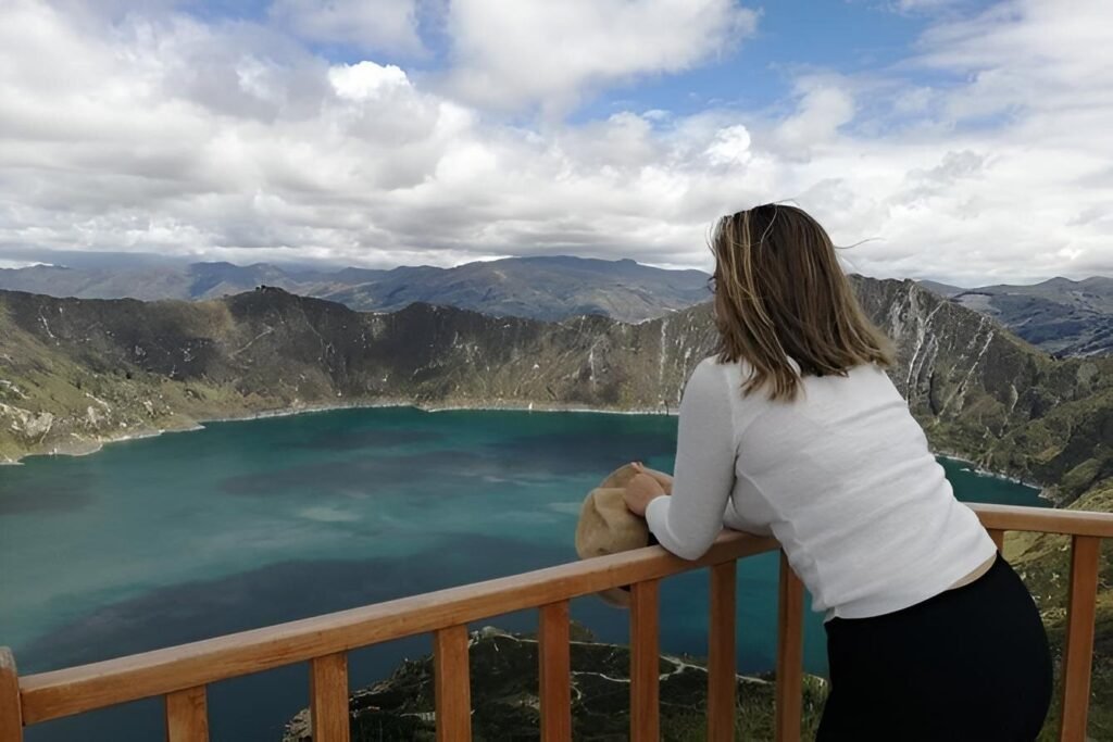 A woman in a white top looks out over Quilotoa Lake from a viewpoint in Ecuador