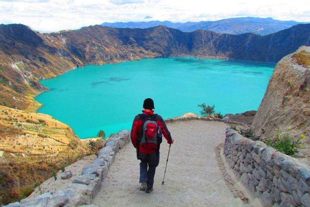 A person walks along a stone path towards the emerald Qulotoa Lake, Ecuador