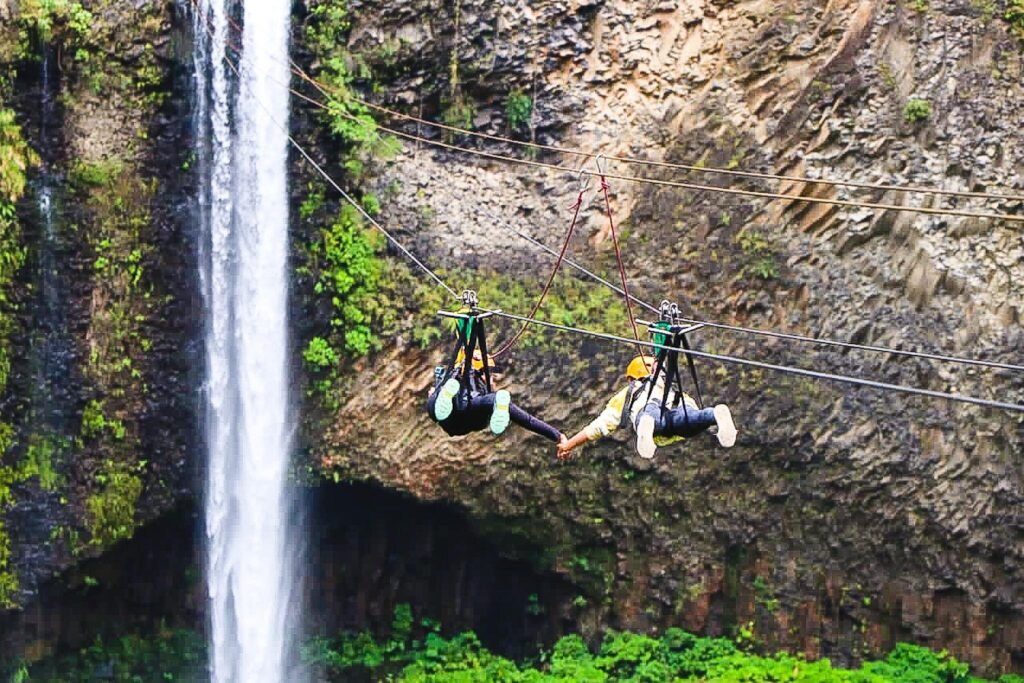 People fly through the air towards a waterfall on a zipline in Baños, Ecuador
