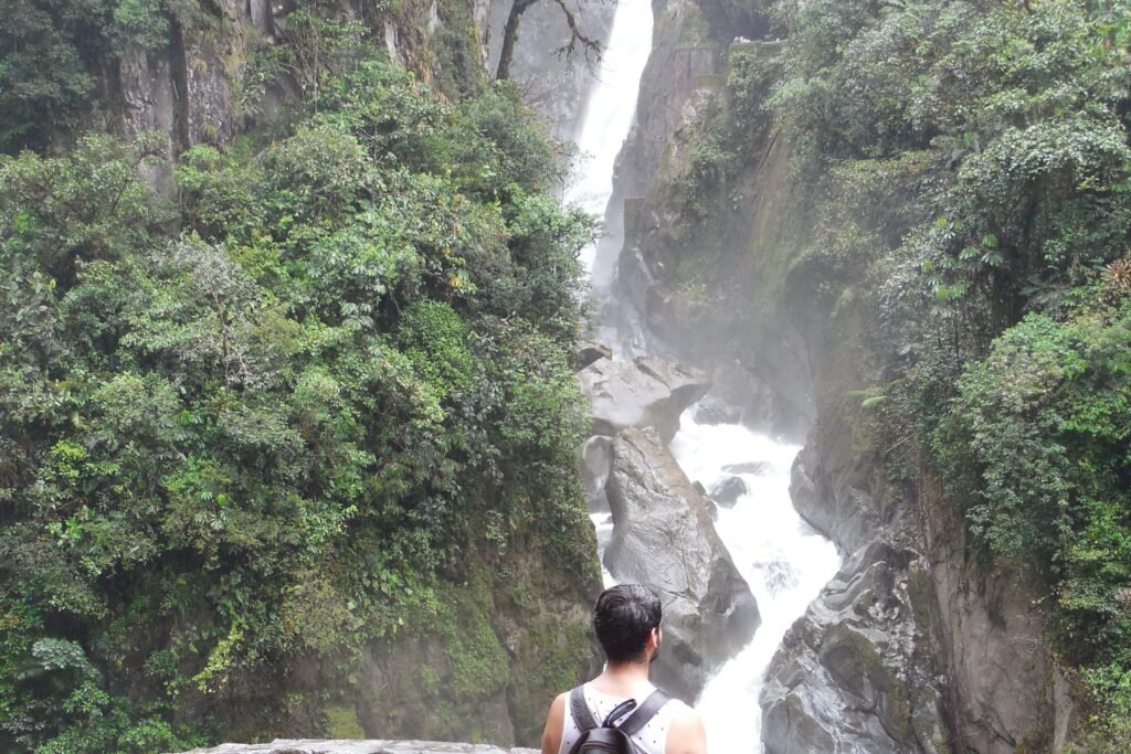 A person looks out at the Pailon del Diablo from a stone balcony near Baños. Wheely Tyred Best bike tours in Ecuador