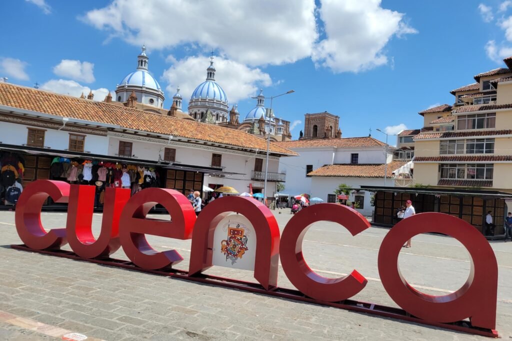 The domes of the New Cathedral can be seen behind a sign reading Cuenca, in Ecuador