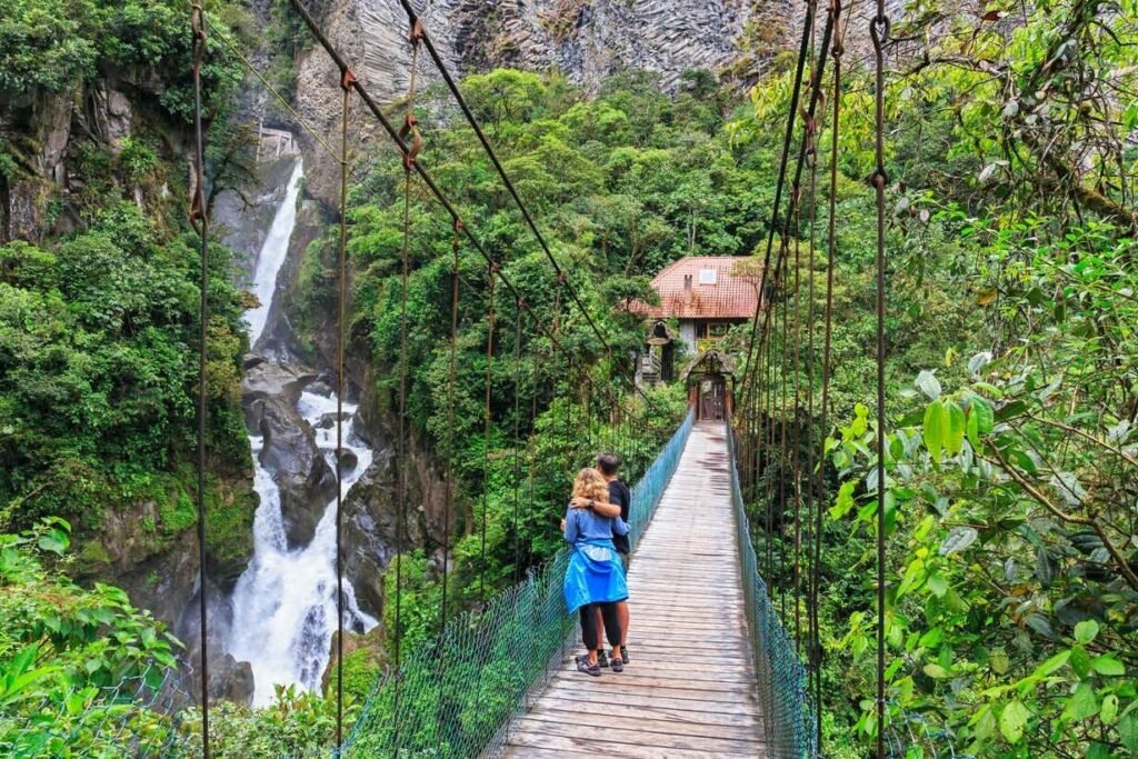 A couple hug and watch a waterfall from a small suspension bridge near Baños. Wheely Tyred Best Ecuador Sierra multi-day tours