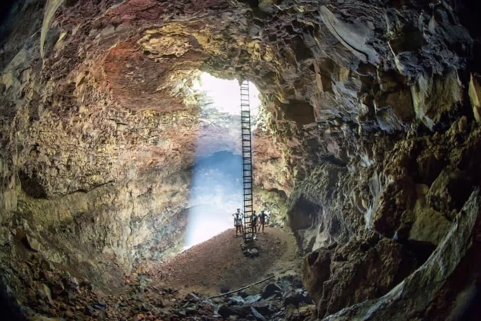 People stand in a lava tube under an exit point that is filled with light under Volcán Trillizos, Isla Isabela, Galápagos