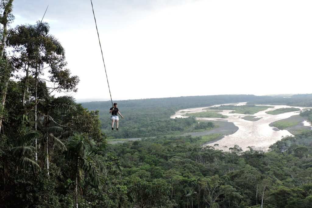 A person swings on a rope high above a valley full of trees and a river near Puyo, Amazon, Ecuador