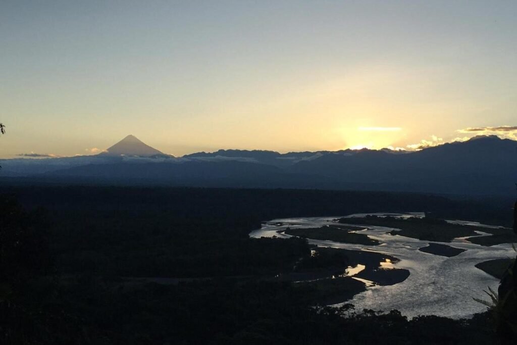 An aerial shot of the Amazon basin at dusk, showing the rainforest, a river, and a volcano in Ecuador