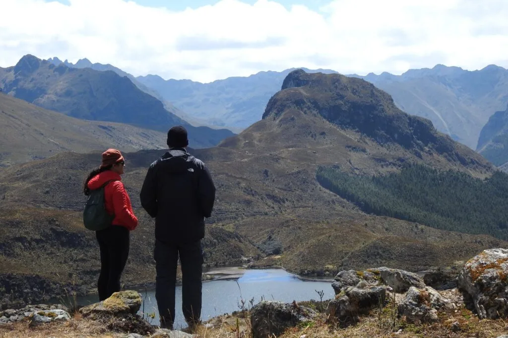 Two people stand and look out over a lake surrounded by mountains in Cajas National Park, near Cuenca, Ecuador