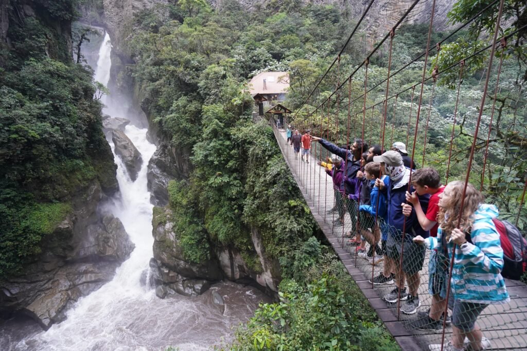 Tourists cross a rope beidge beside the huge Pailon Del Diablo waterfall in Baños, Ecuador. Wheely Tyred Best Multi-Day Tours from Quito