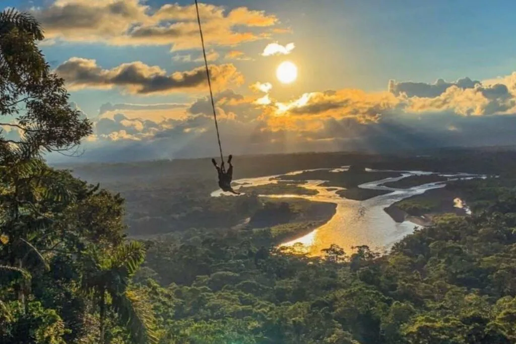 A man swings above the jungle as the sun sets near Baños, Puyo, Ecuador