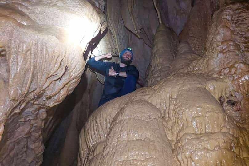 A man stands in Los Tayos Cave by some rock formations with a head torch on near Baños, Ecuador