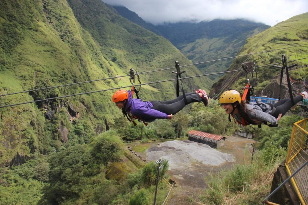 Two people fly through a river valley attached to a cable near Baños, Ecuador