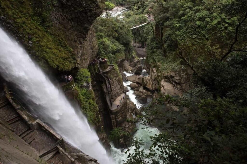 The huge waterfall of Pailon Del Diablo tumbles into a canyon as people climb a rocky path up the side, in Baños, Ecuador