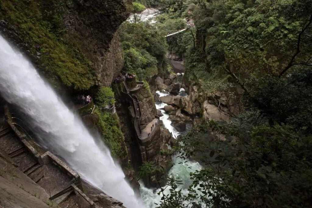The huge waterfall of Pailon Del Diablo tumbles into a canyon as people climb a rocky path up the side, in Baños, Ecuador