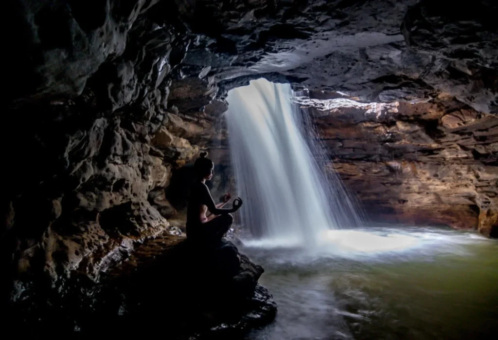 A woman sits in the lotus position in a cave with a waterfall near Tena, Ecuador