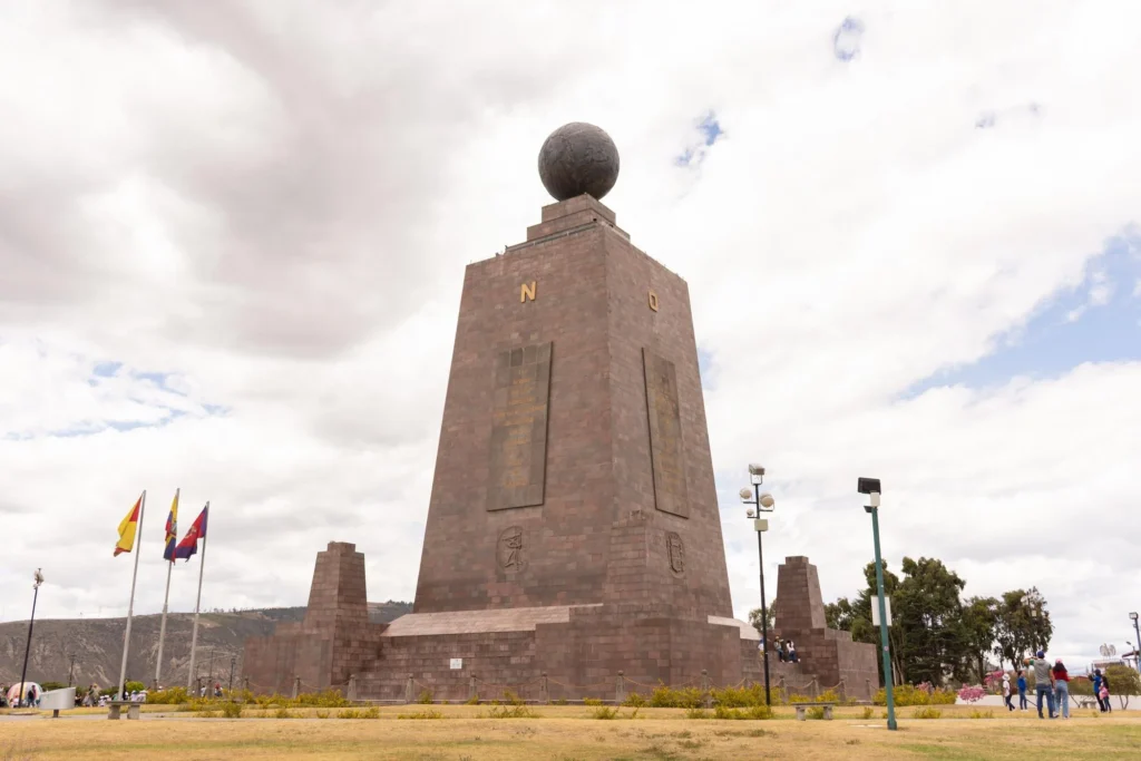 The huge Mitad del Mundo monument towers over flags and buildings. It has a globe on top, representing the Equator, in Quito Ecuador