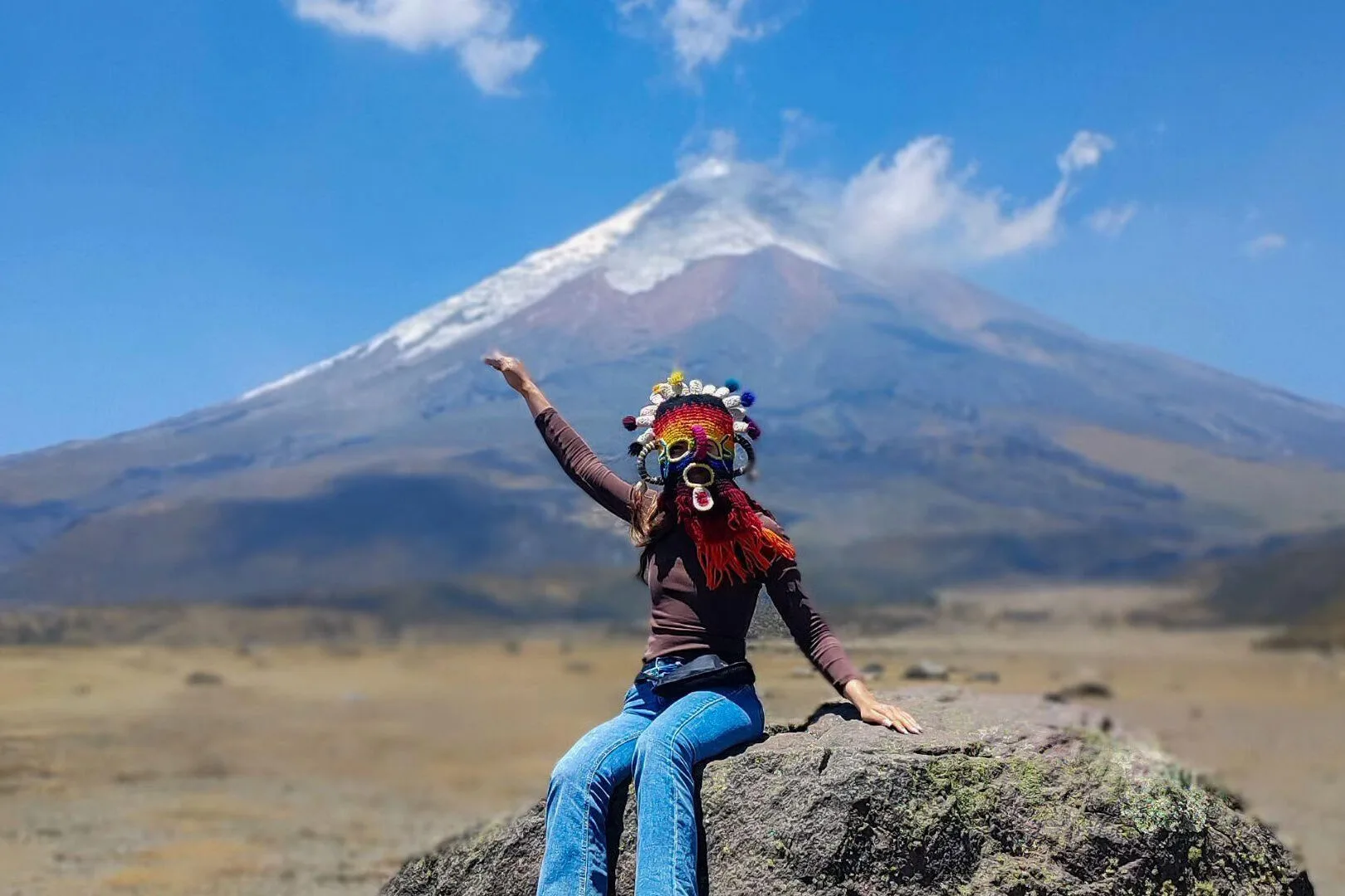 A woman poses in an Ecuadorian Aya Huma mask in front of Cotopaxi, Ecuador